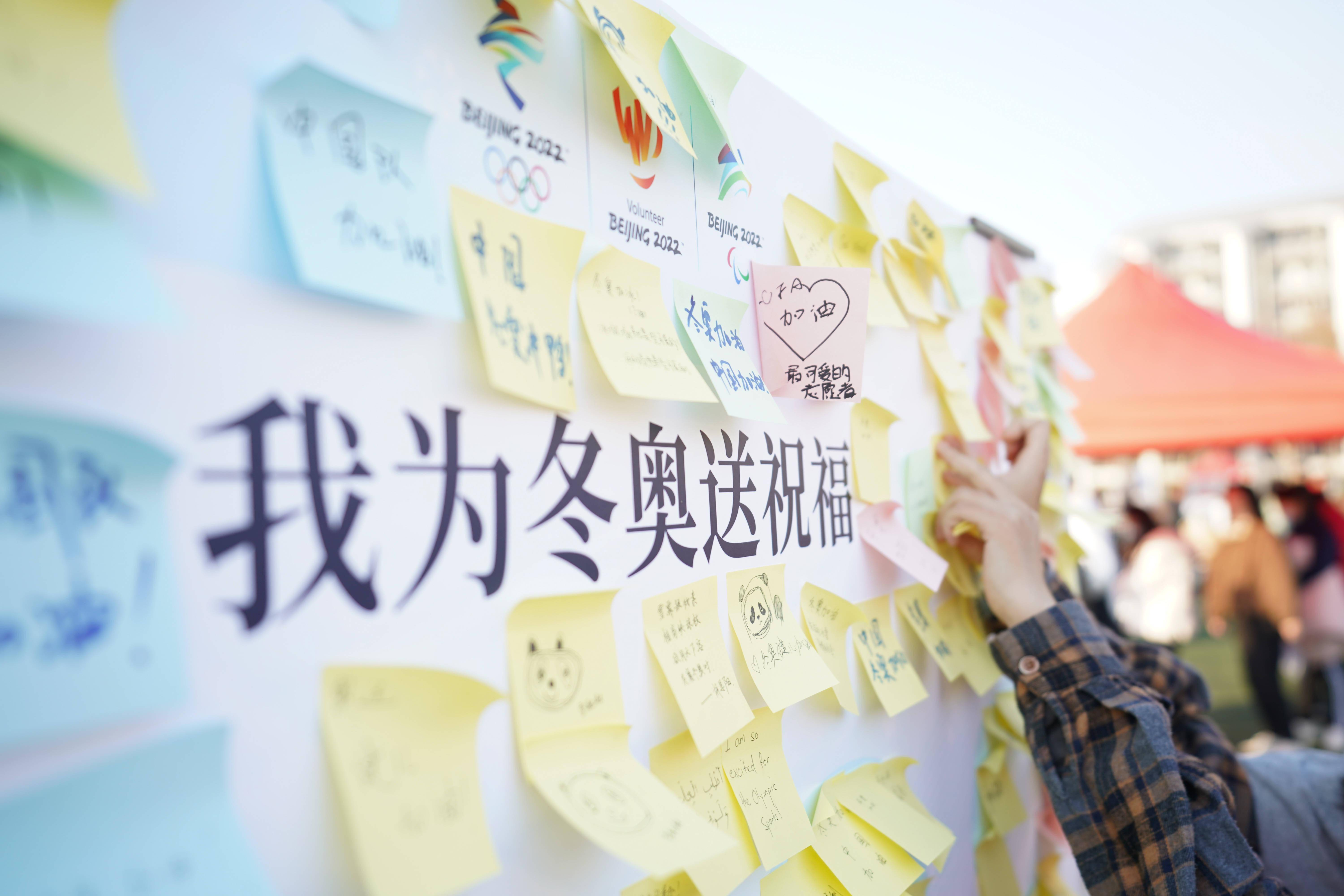 一位学生在活动现场的"我为冬奥送祝福"宣传板上贴上自己的祝福语