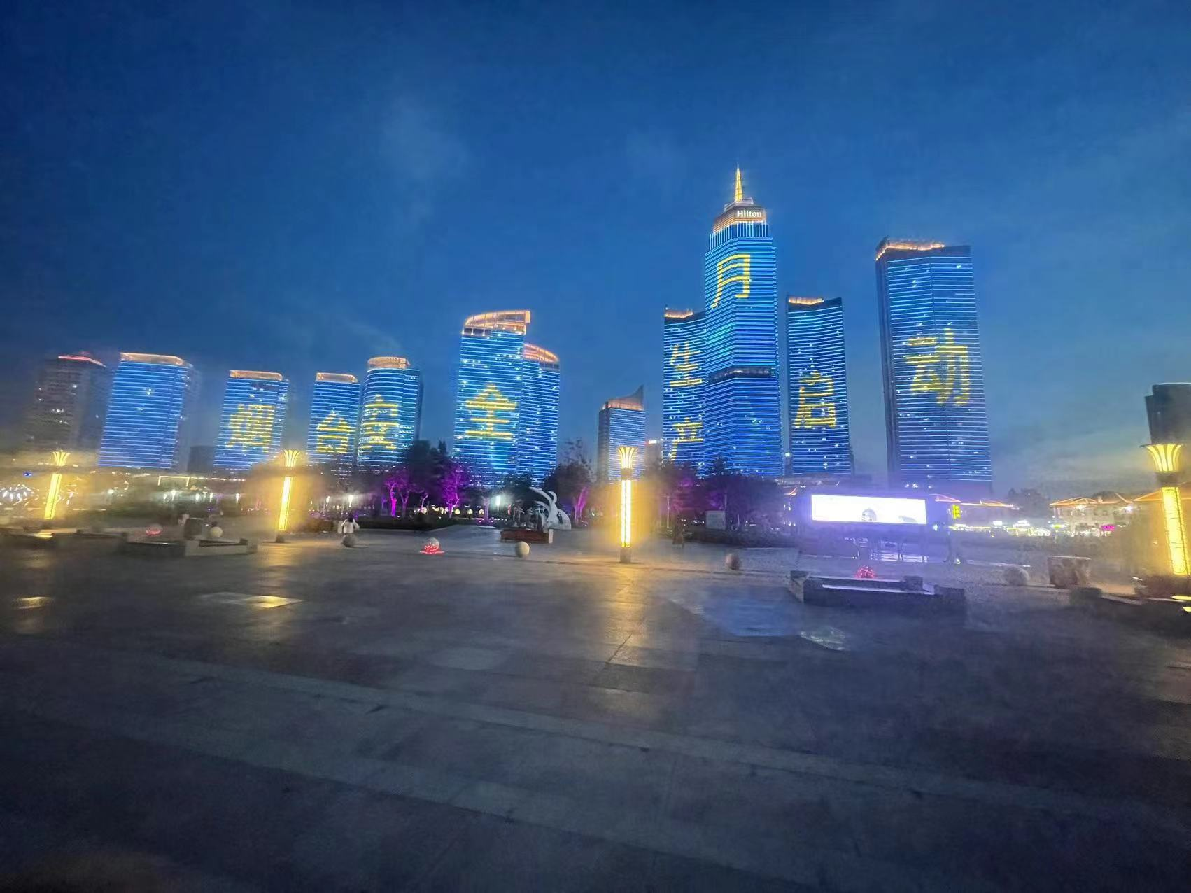 条宣传标语会闪耀在滨海广场建筑物外墙上,画面铺满高楼,融入夜景之中