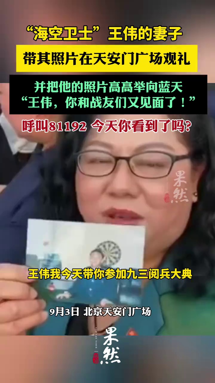 “海空卫士”王伟的妻子阮国琴在观礼台上把王伟的照片举向蓝天（央视新闻、极目新闻）